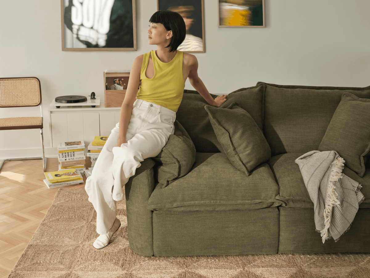 Koala Tamarama 2-section modular sofa in Forest Walk, with model, brown knit cushion and bookshelves backdrop