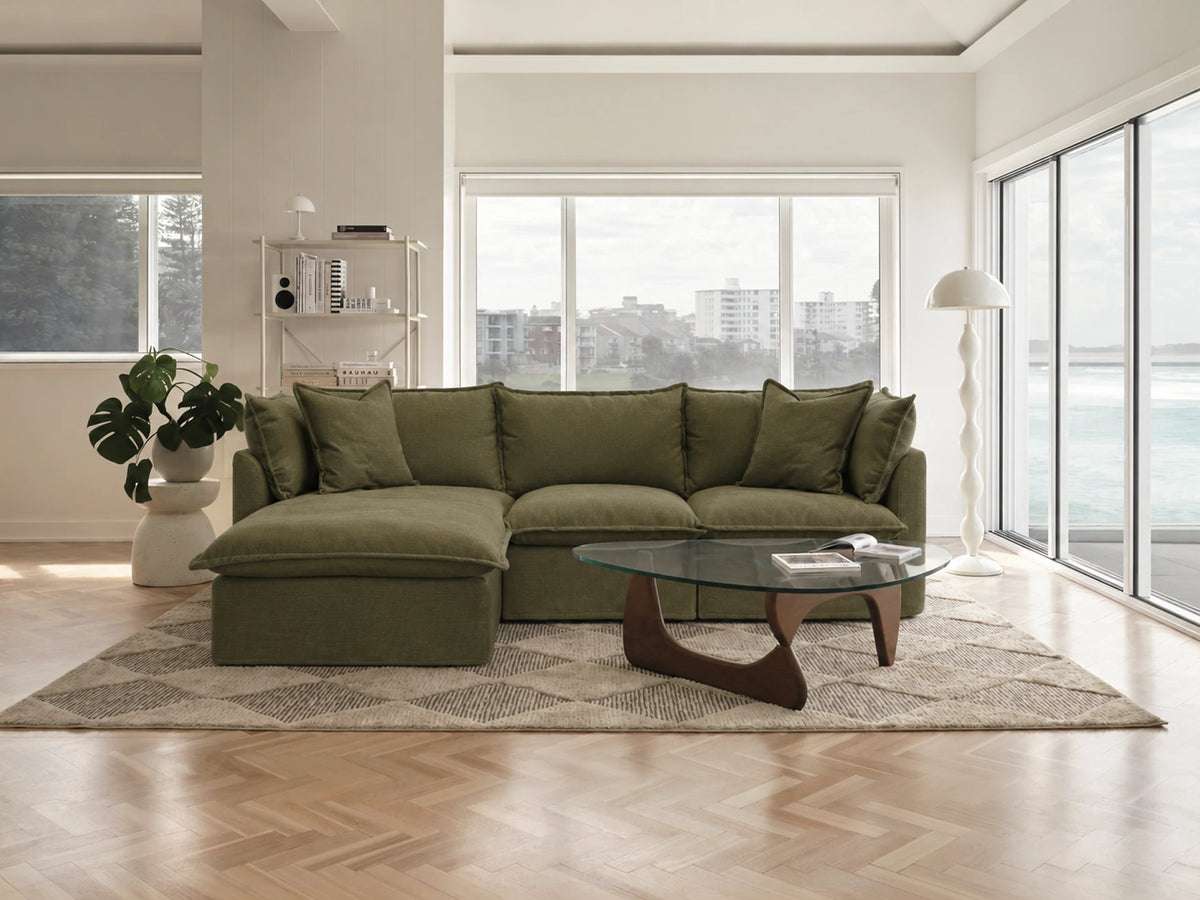 Modern living room with a green sectional sofa, coffee table, and large windows.