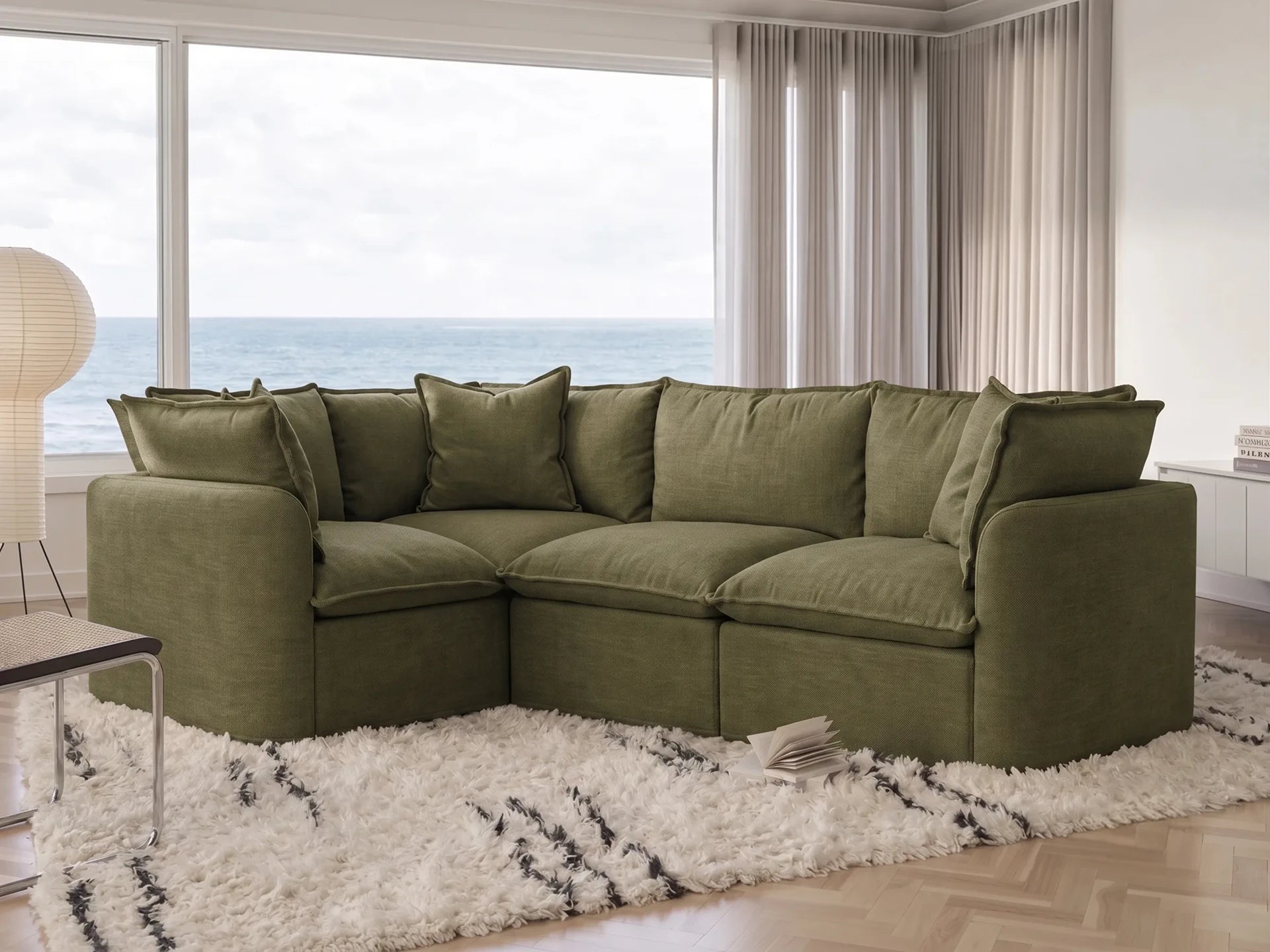 Green sectional sofa in a living room with large windows and ocean view.