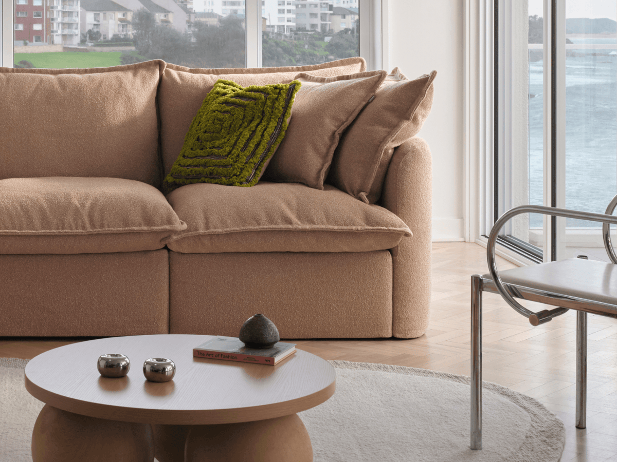 Koala Tamarama 4-section L-shape sectional in Pebble Beach, with model, brown knit cushion and bookshelves backdrop