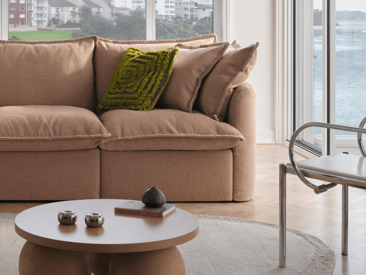 Koala Tamarama 4-section L-shape sectional in Pebble Beach, with model, brown knit cushion and bookshelves backdrop