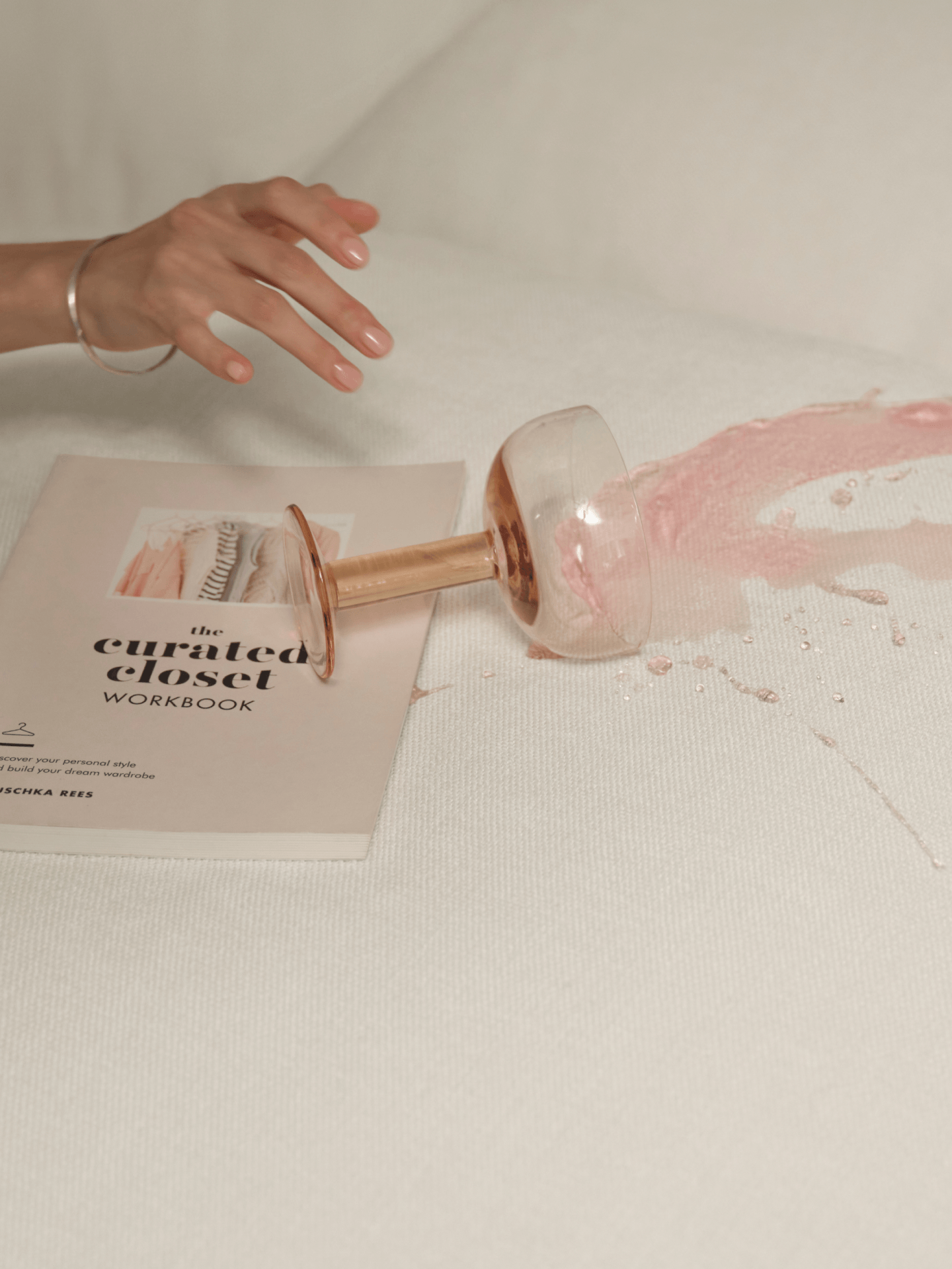 Glass bottle with pink liquid on a textured surface next to a book titled 'The Curated Closet Workbook'.