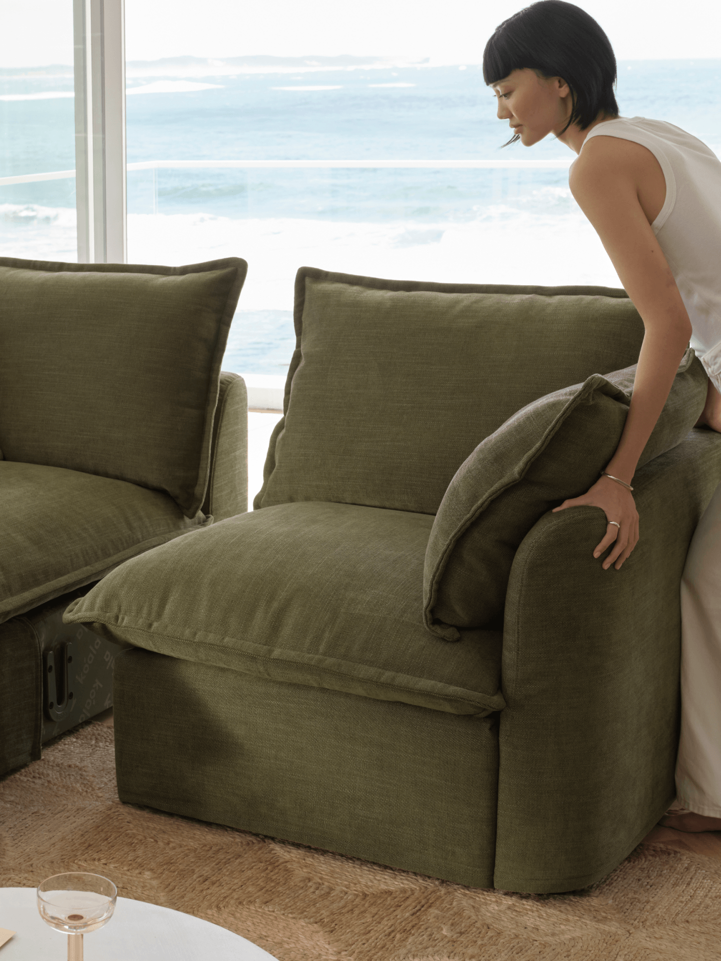 Woman sitting on a green sofa in a bright room with large windows.