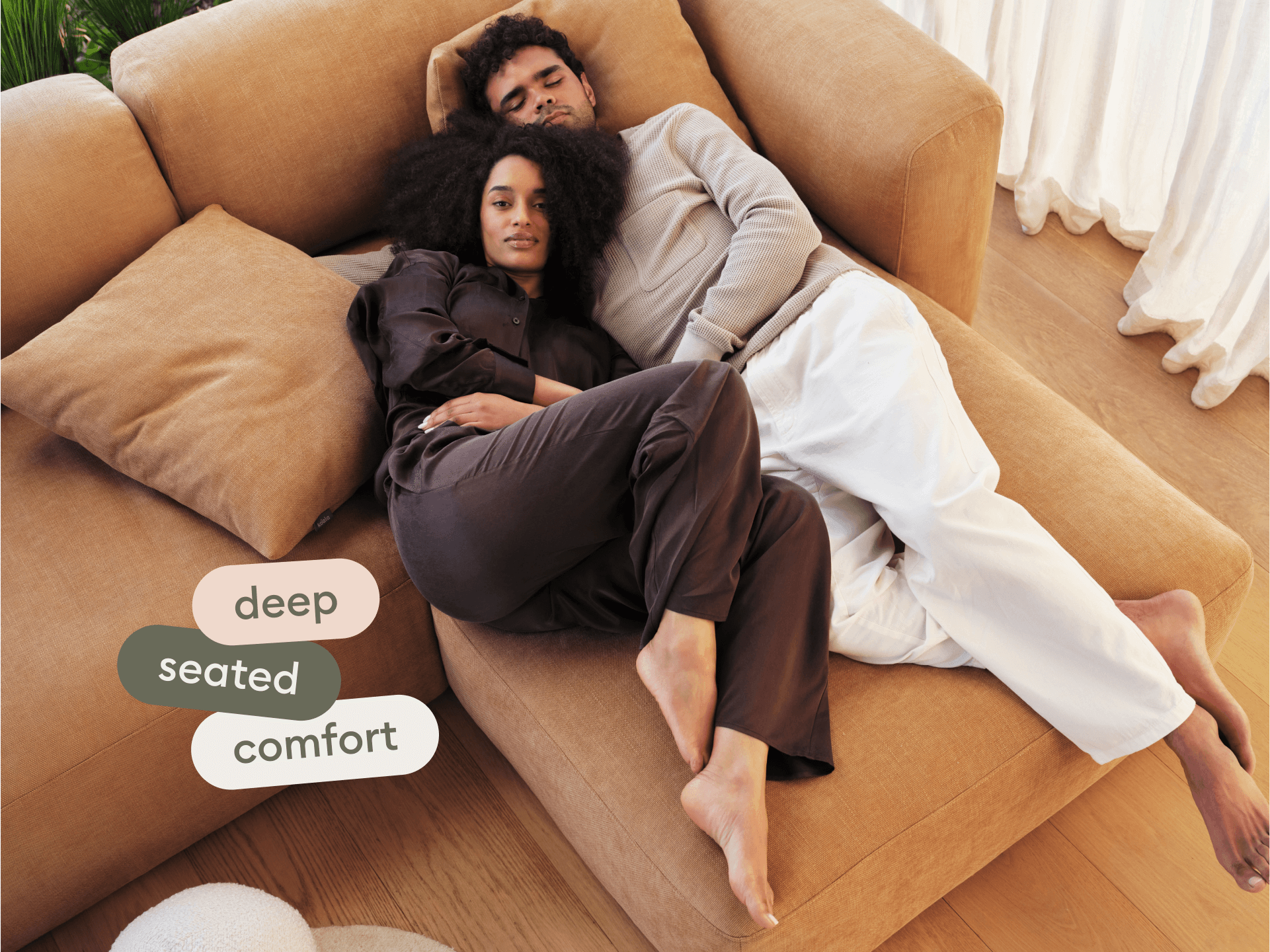 Modern sectional sofa in caramel suede fabric, featuring deep seating and plush cushions. Set on light hardwood floor in a sunlit, minimalist living area.