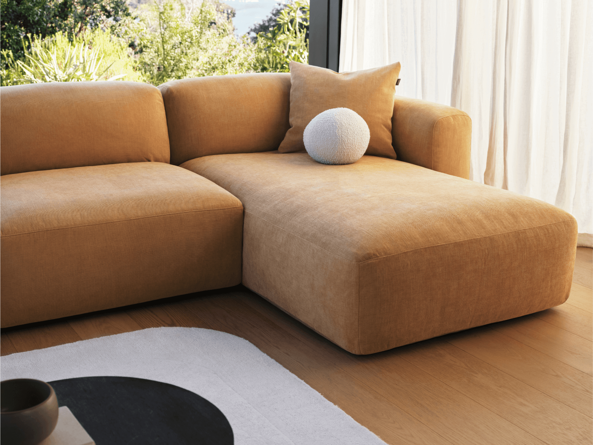 Luxurious tan velvet sectional sofa with chaise lounge. Features deep seating, plush cushions, and a minimalist silhouette in a sunlit living room setting.