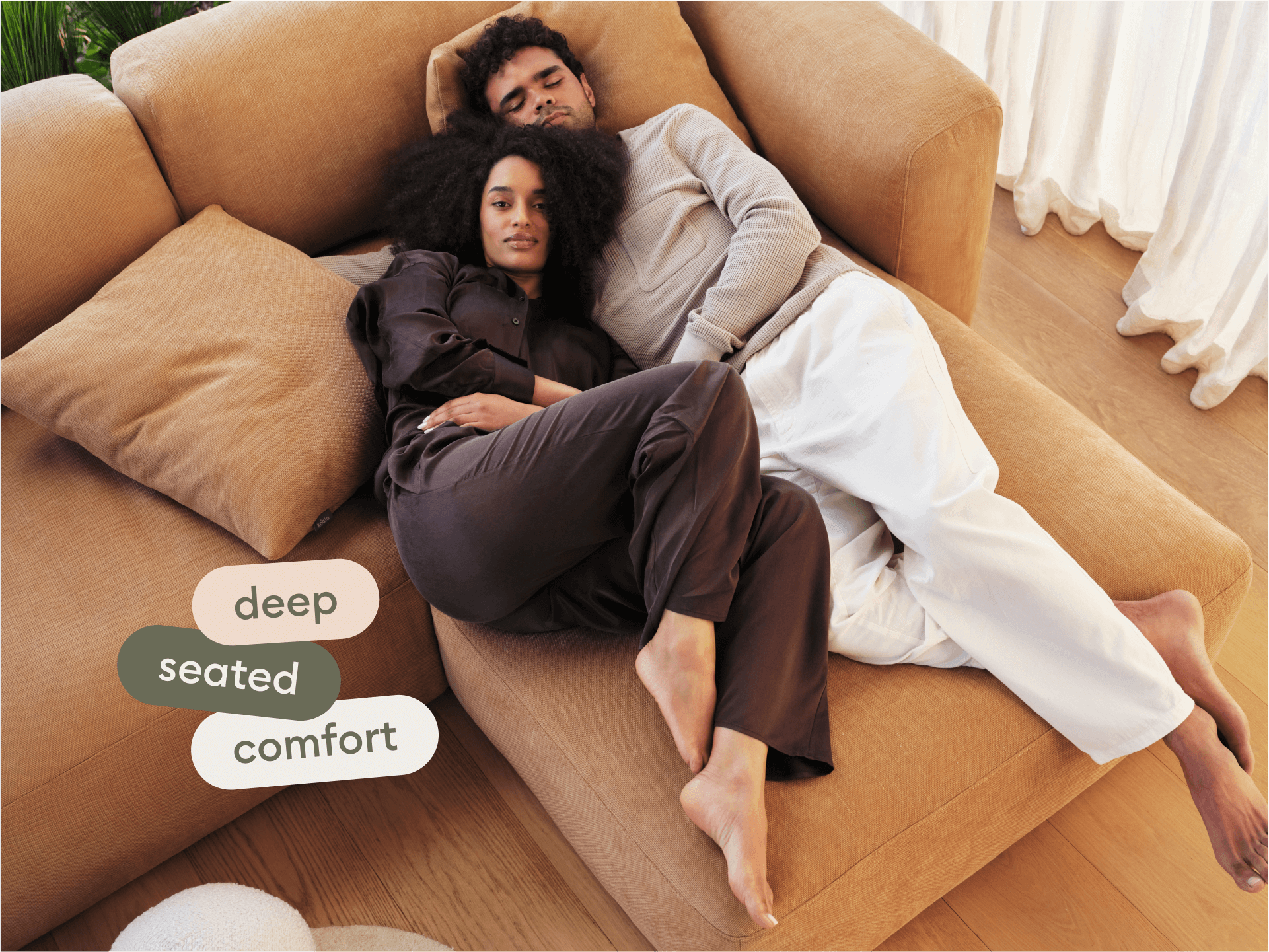 Luxurious beige sectional sofa in plush fabric, featuring deep seating and clean lines. Set in a minimalist room with warm wood flooring and sheer curtains.