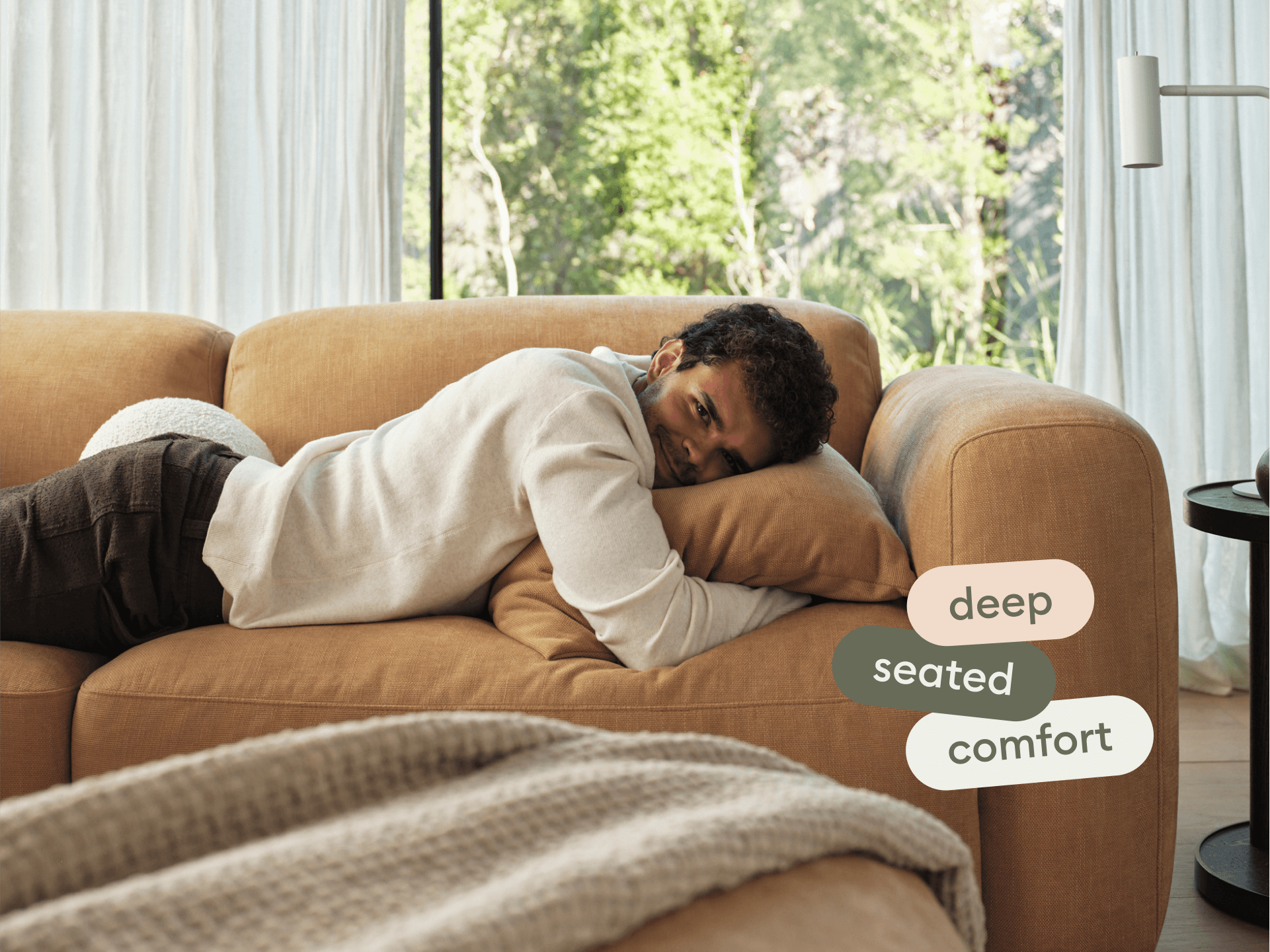 Luxury caramel leather sofa with deep seating, plush cushions, and sleek curved arms. Set in a spacious, light-filled living room with floor-to-ceiling windows.