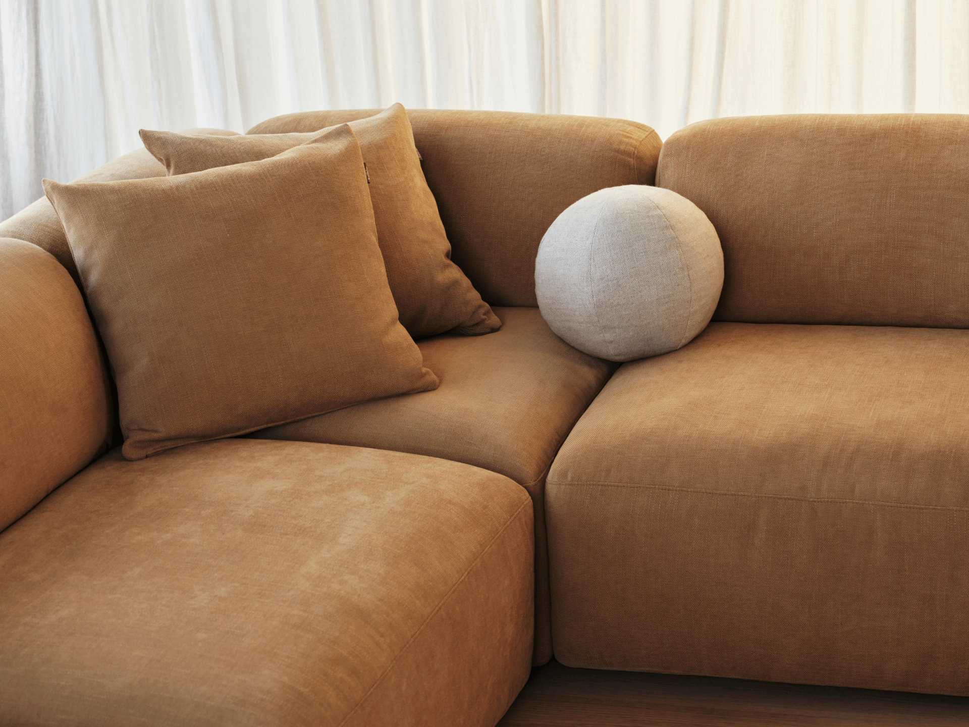 Luxurious caramel velvet sectional sofa with plush cushions. Set in a warmly lit room, it exudes cosiness and contemporary elegance.