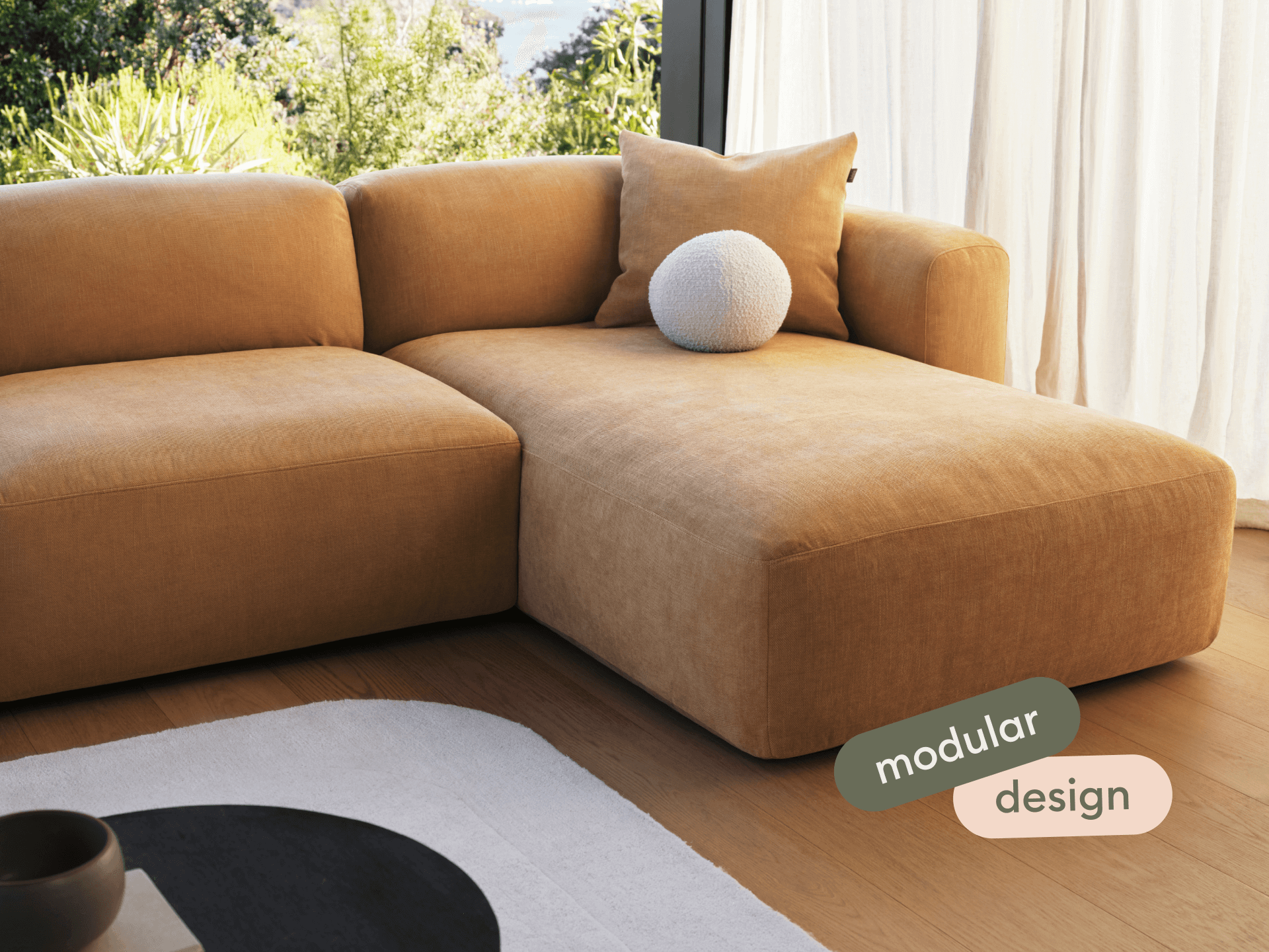 Luxurious modular sofa in rich caramel fabric, featuring a plush chaise and sleek lines, set in a sunlit living room with floor-to-ceiling windows.