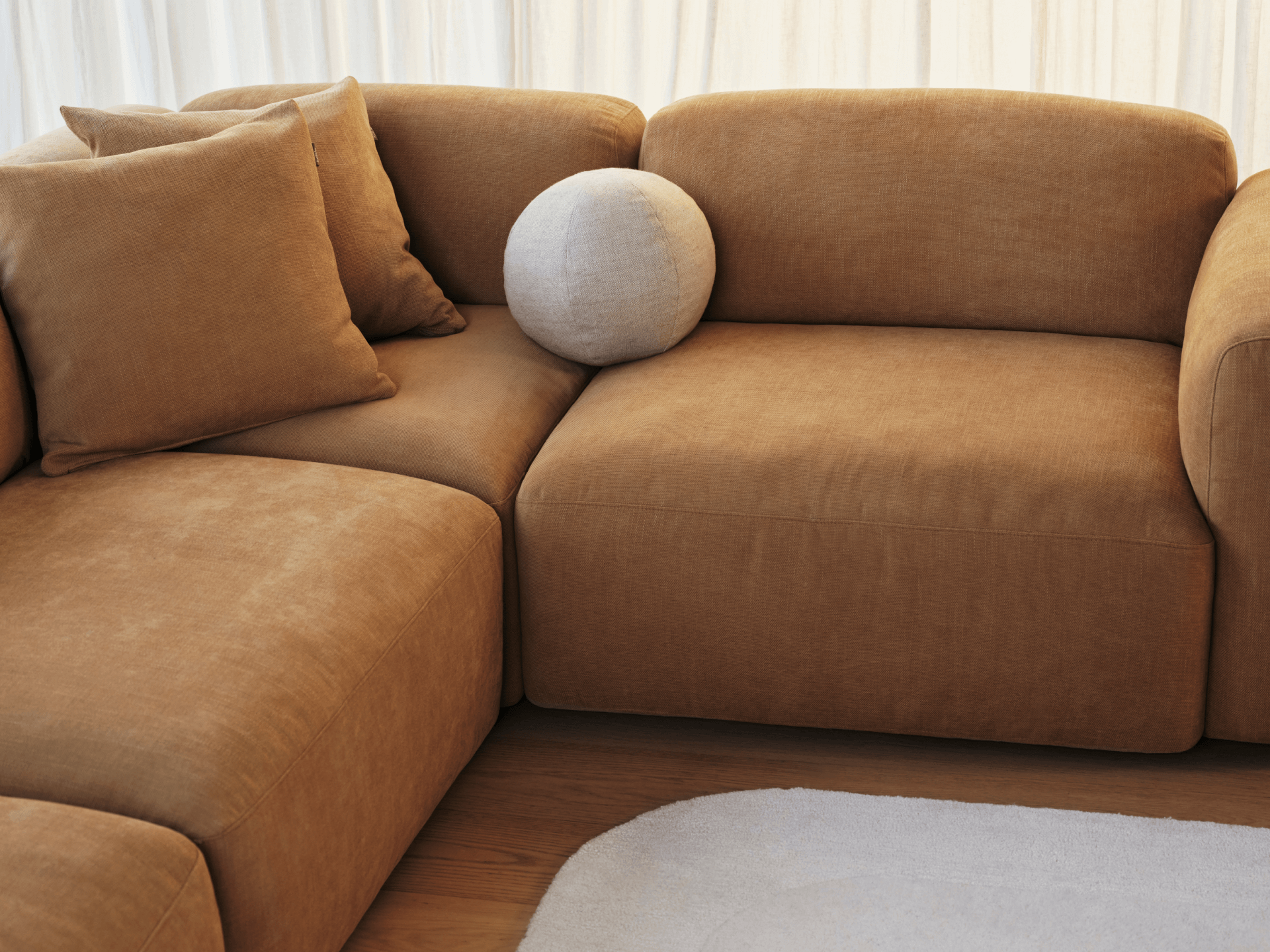 Luxury modular sofa in plush caramel velvet, featuring low backrests and deep seating. Paired with neutral cushions in a sunlit, minimalist living room.