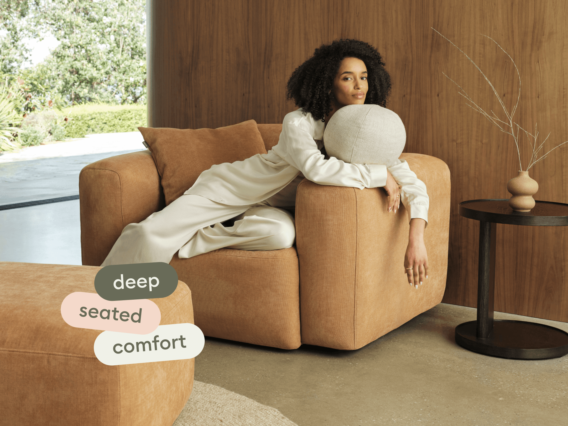 Luxurious tan suede armchair with deep seating, complemented by a matching ottoman. Set in a minimalist, open-concept space with natural wood accents.