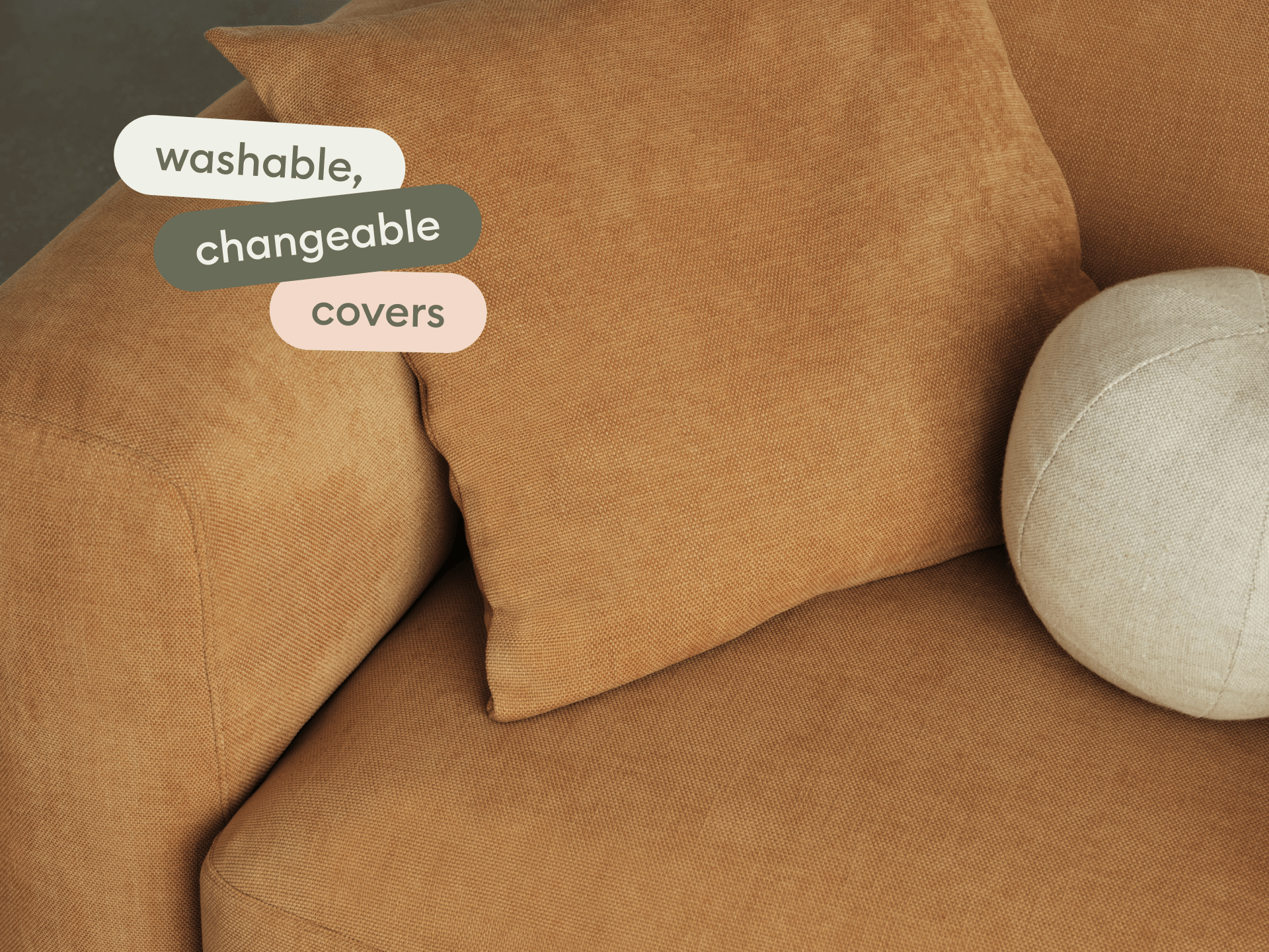 Modern sofa with washable, changeable covers in a warm terracotta hue. Features plush cushions, textured fabric, and rounded edges. Elegant lounge setting.