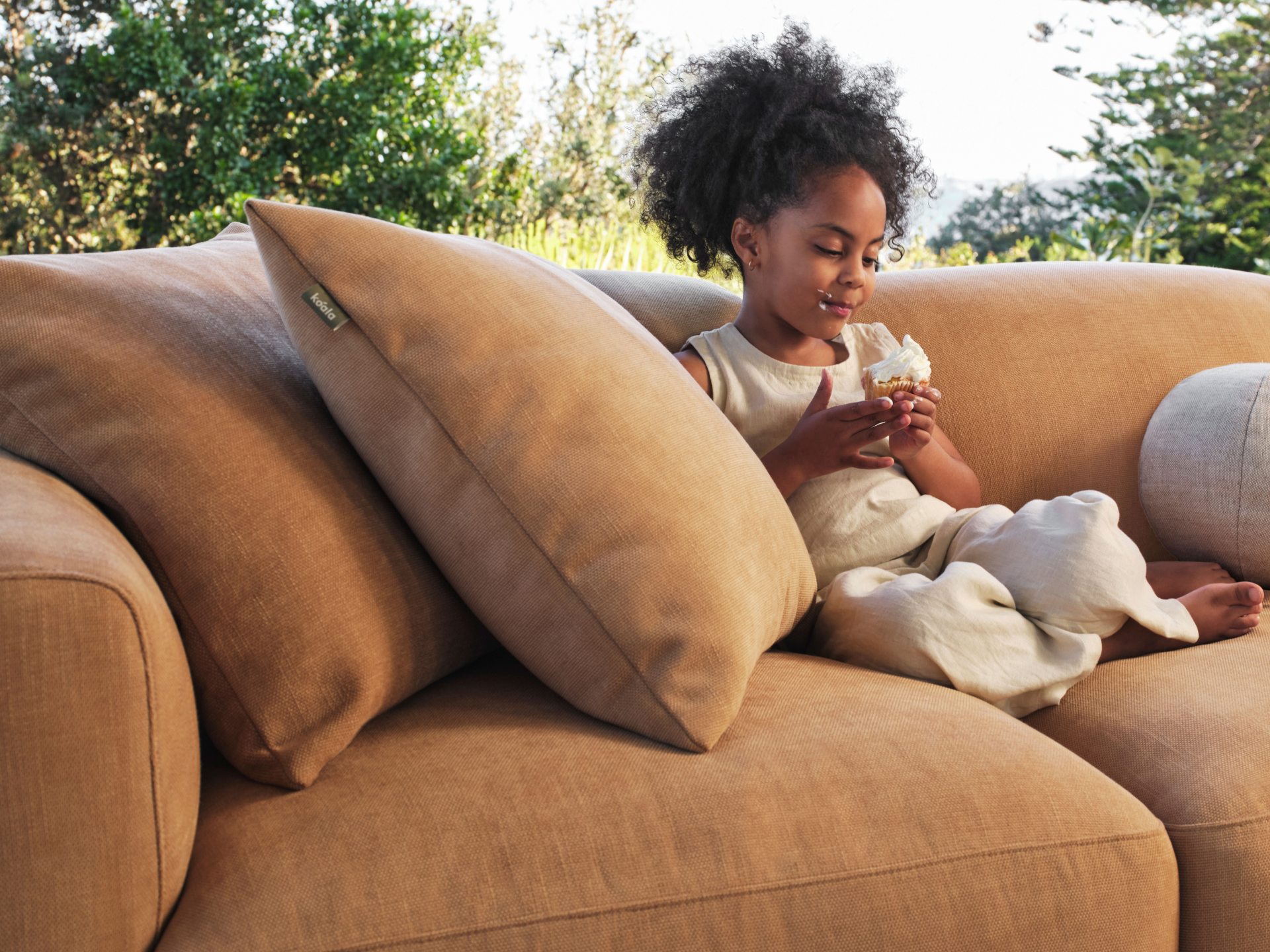 Luxury tan linen sofa, plush cushions, curved armrests, set in outdoor garden. Elegant, contemporary design, ideal for sophisticated alfresco spaces.
