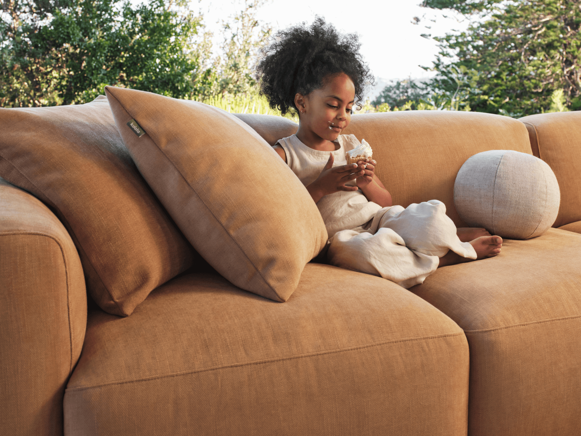 Plush tan sectional sofa in soft linen fabric, featuring oversized cushions and relaxed seating, set in a lush outdoor garden for a chic, modern look.