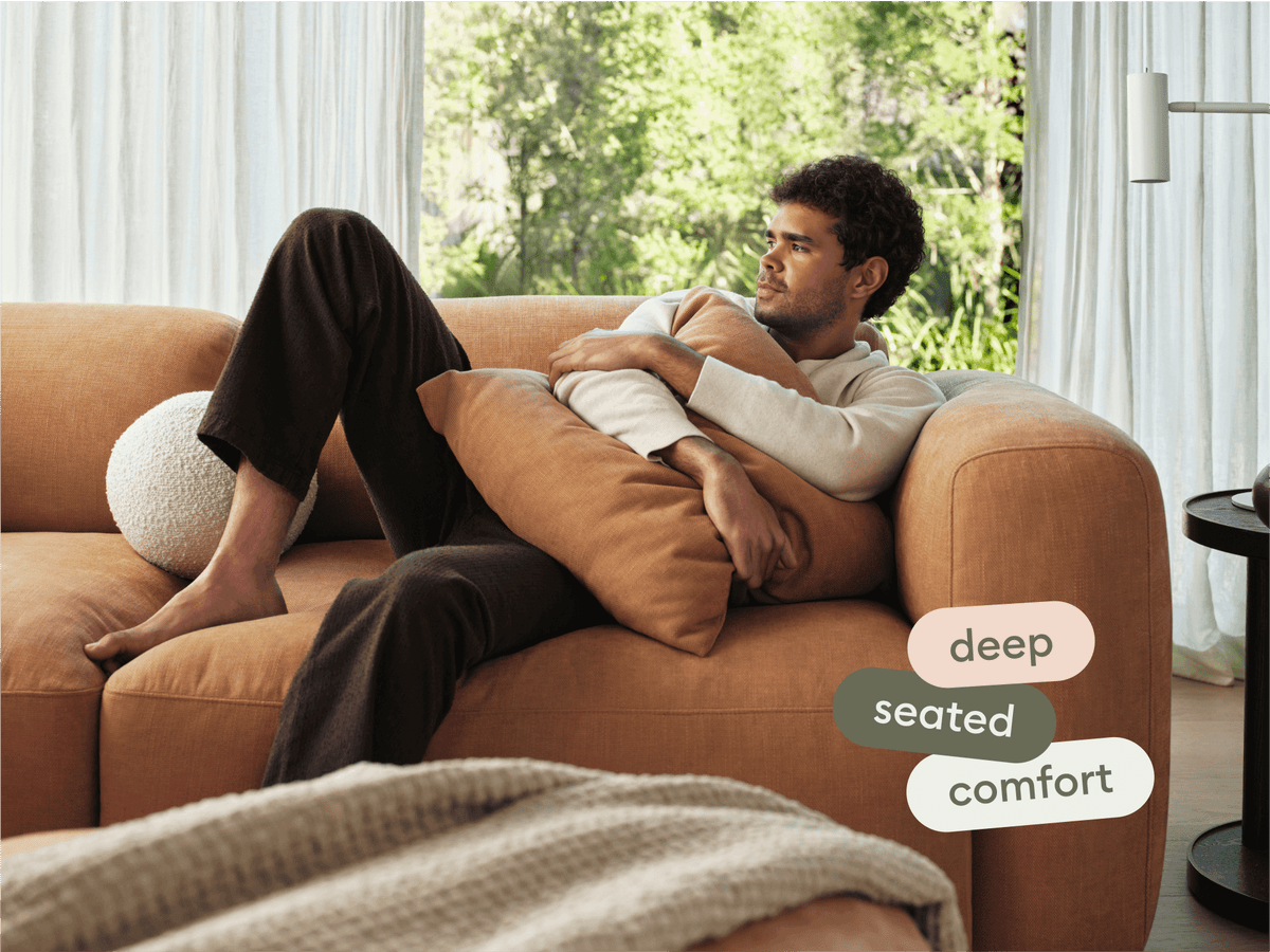 Modern caramel velvet sofa with deep seating, plush cushions, and soft curves. Set in a stylish living room with natural light and greenery view.