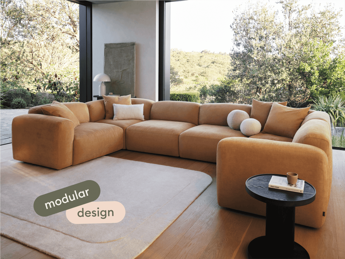 Luxurious mustard modular sofa in soft fabric, featuring deep seats and plush cushions. Set in a modern living space with floor-to-ceiling windows.