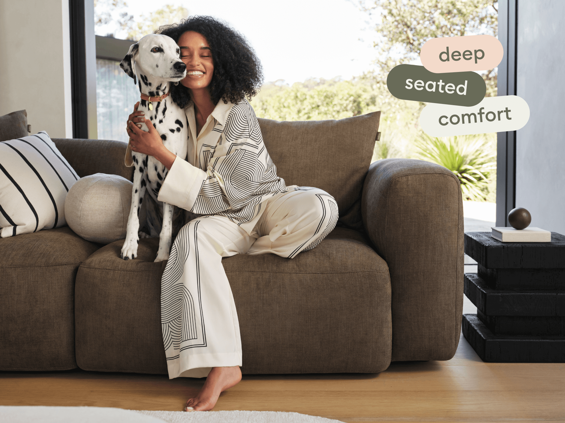 Luxurious deep-seated sofa in rich chocolate brown fabric, featuring plush cushions and wide armrests, set in a sunlit, modern living room.