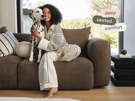 Plush, deep-seated sofa in rich mocha fabric, featuring broad, cushioned arms and a minimalist design, set in a sunlit, modern living room.