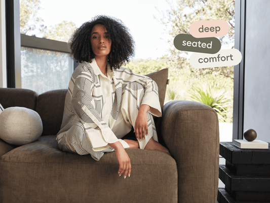 Luxurious deep-seated sofa in rich brown fabric, showcasing plush cushions and wide armrests. Set in a bright, modern living space with garden views.