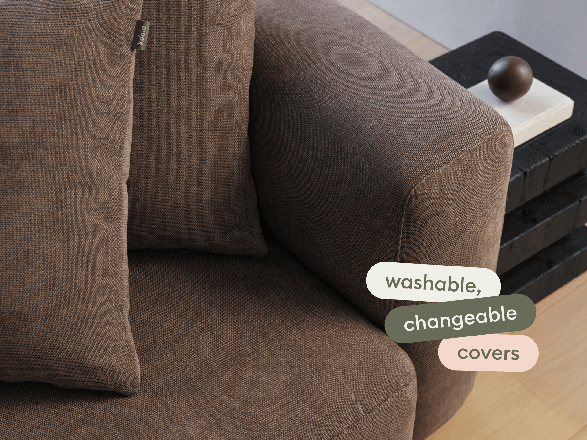 Brown linen sofa featuring washable, changeable covers. Modern armrest design in a sleek living space with light wooden floors.