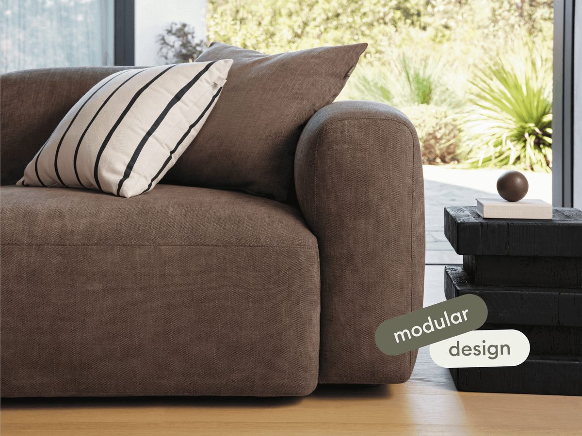 Luxurious modular sofa in rich brown fabric, featuring plush cushioning and rounded armrests. Set in a modern living space with natural light.
