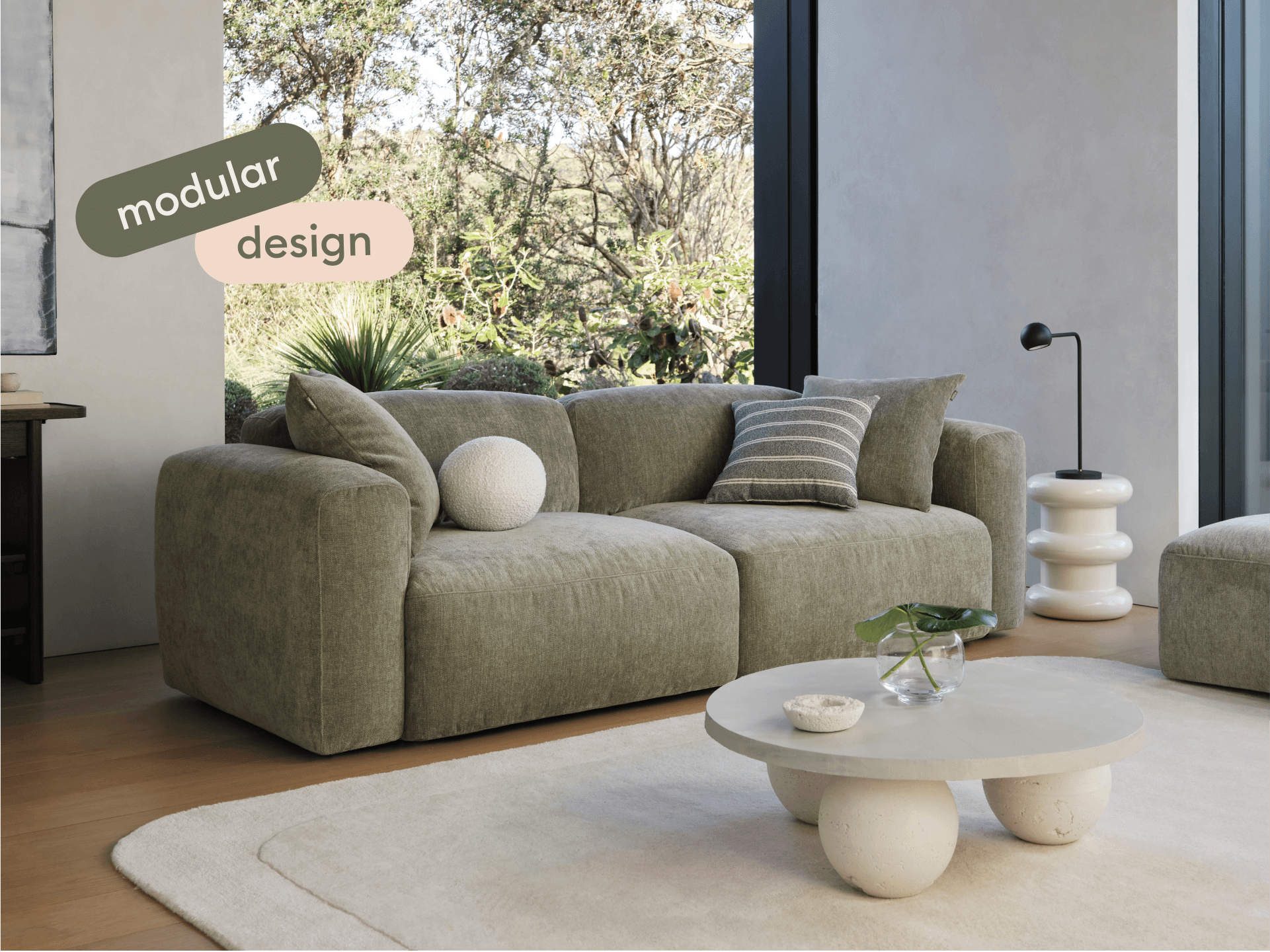 Luxurious modular sofa in neutral taupe fabric, featuring plush cushions and deep seating. Positioned in a sunlit modern living room with wooden floors.