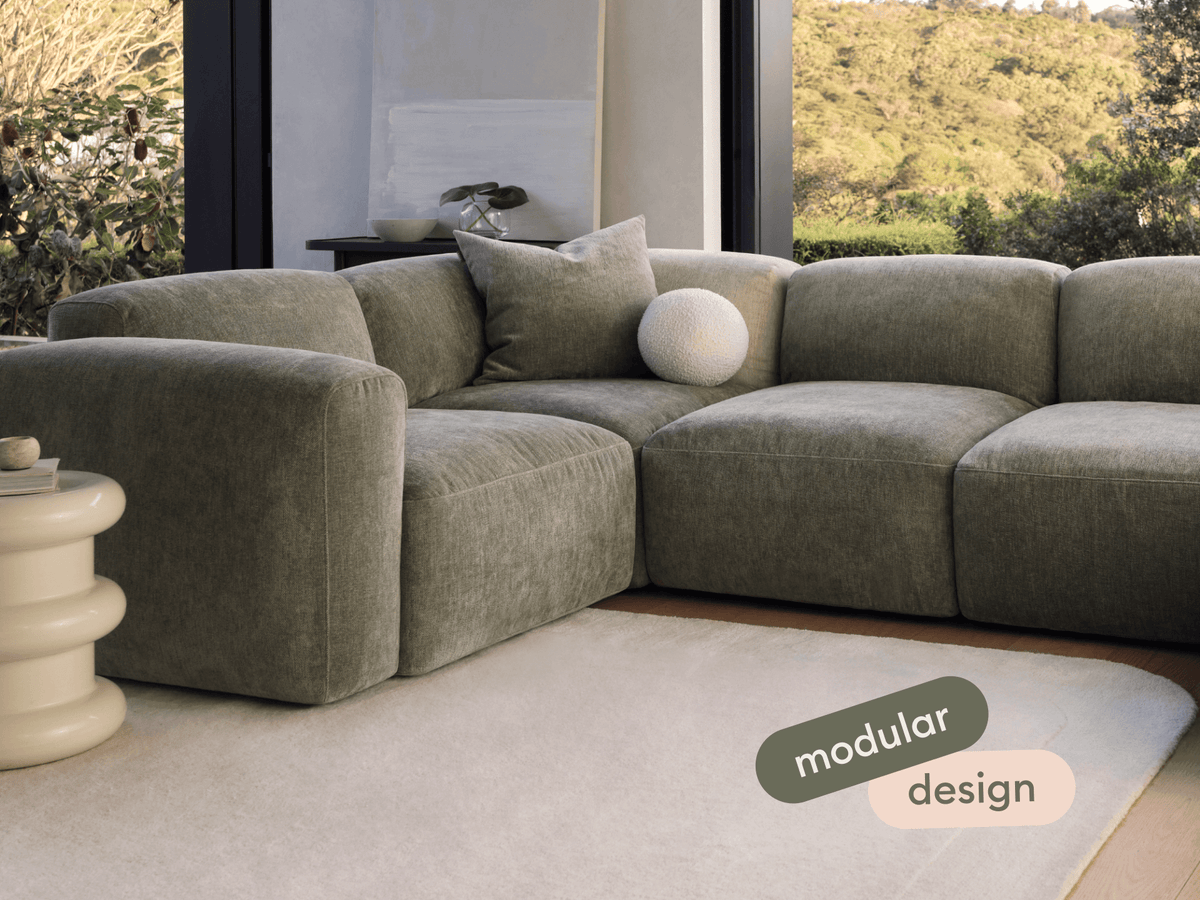 Luxurious modular sofa with plush, olive-green velvet upholstery. Features deep seats, a minimalist design, and a serene living room setting with scenic views.