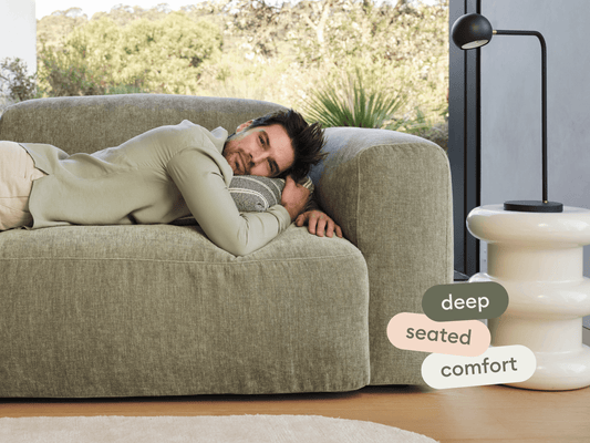 Luxurious deep-seated sofa in textured beige fabric, featuring plush cushions. Positioned next to a sculptural white side table and black lamp in a modern setting.