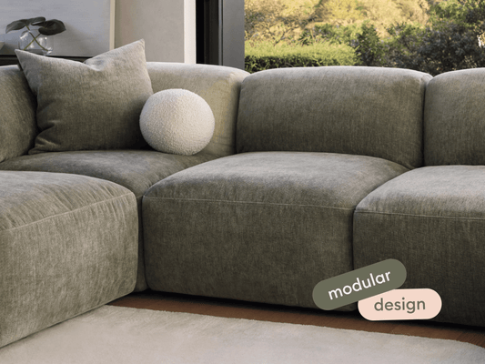 Luxurious modular sofa in soft grey fabric, featuring plush cushions and sleek lines. Set in a modern living space with natural light and garden view.