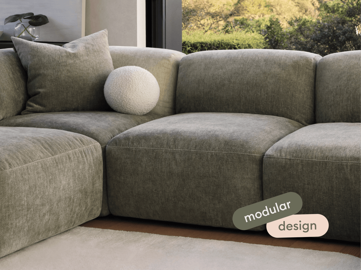 Modular sofa in textured olive fabric, featuring plush cushions and a modern design. Set in a sunlit room with large windows and neutral flooring.
