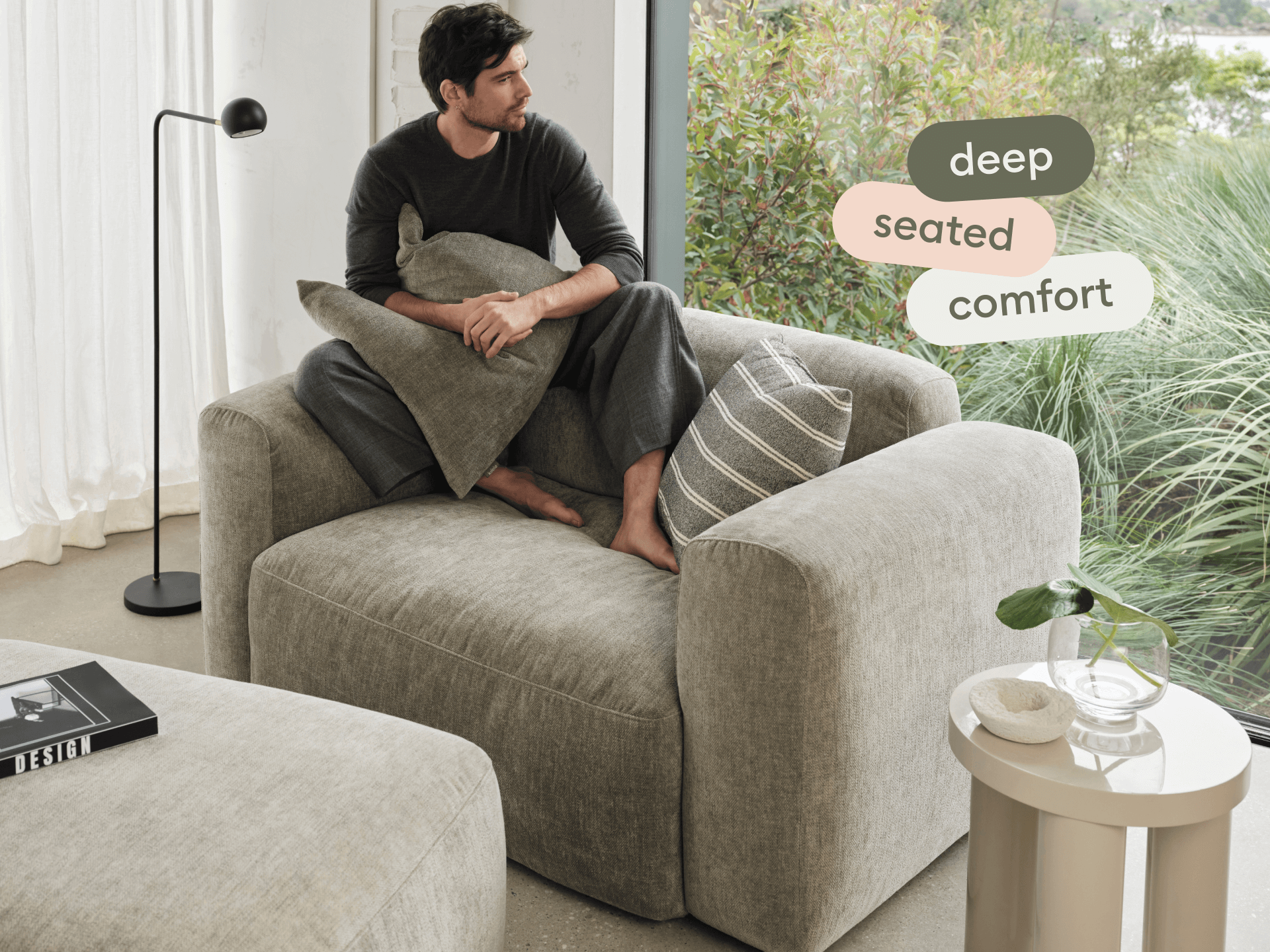 Luxurious grey armchair with plush, deep-seated cushioning in a premium linen finish. Set in a modern room with a floor lamp and glass-side table.