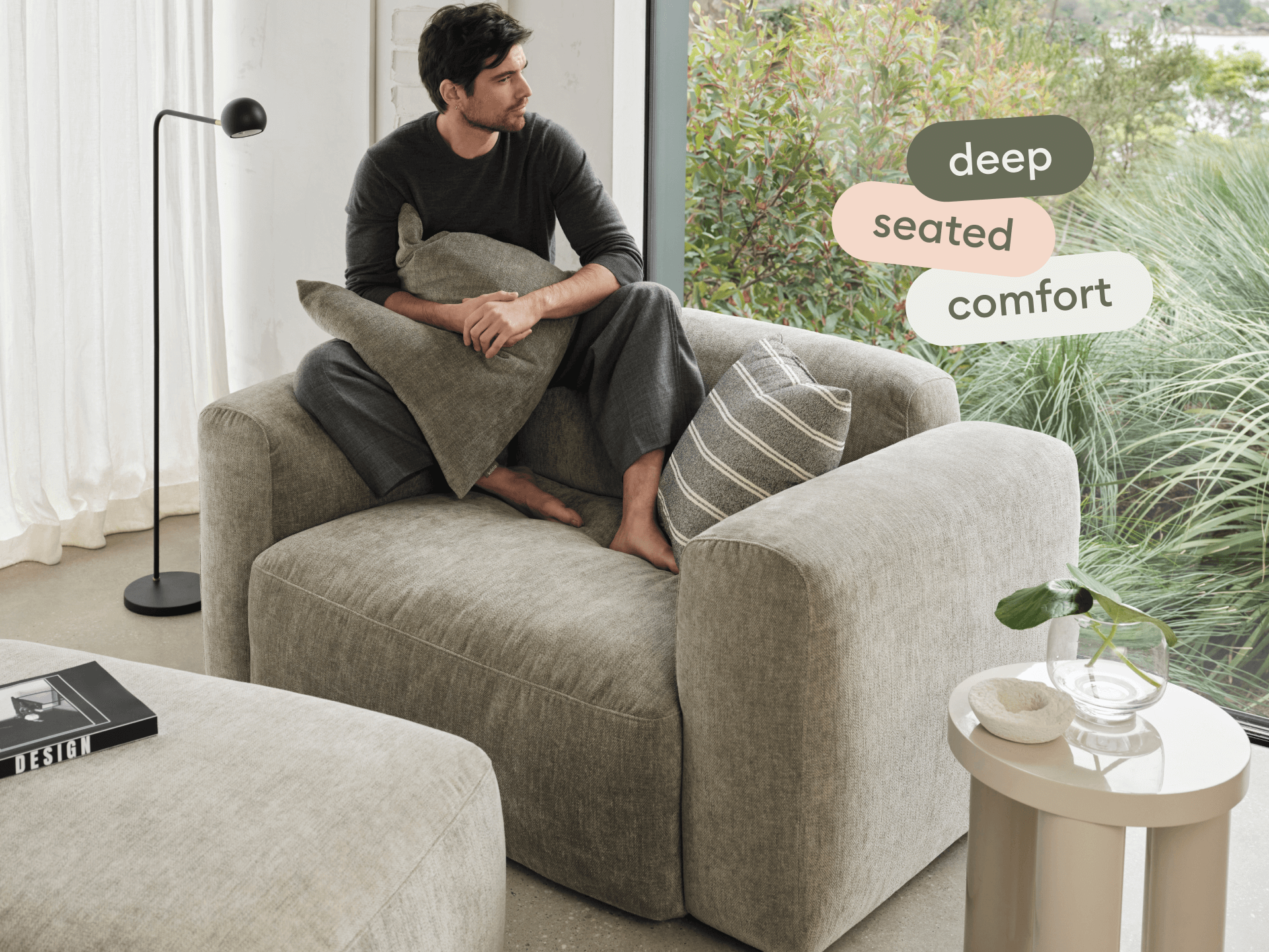 Luxurious grey linen armchair with deep seating, paired with matching ottoman. Features plush cushions and sleek lines, set in a chic, light-filled room.