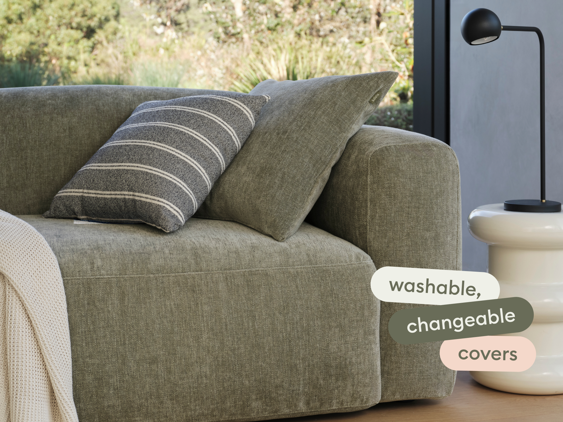 Luxurious olive-green fabric sofa with washable, changeable covers. Features a sleek, modern silhouette, paired with striped and solid cushions. Indoor setting.