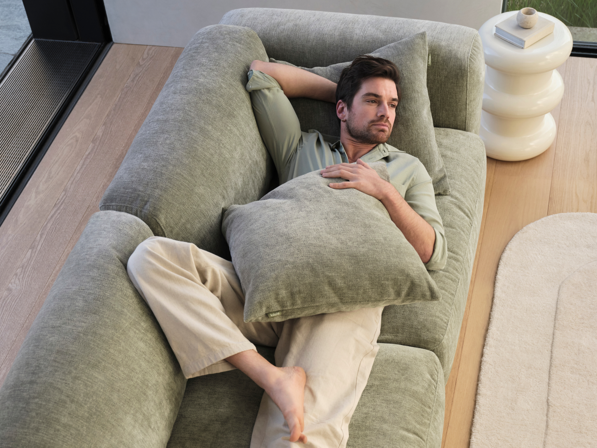 Luxurious L-shaped sofa in muted sage velvet, featuring plush, deep seating and modern design. Positioned in a light-filled, minimalist living space.