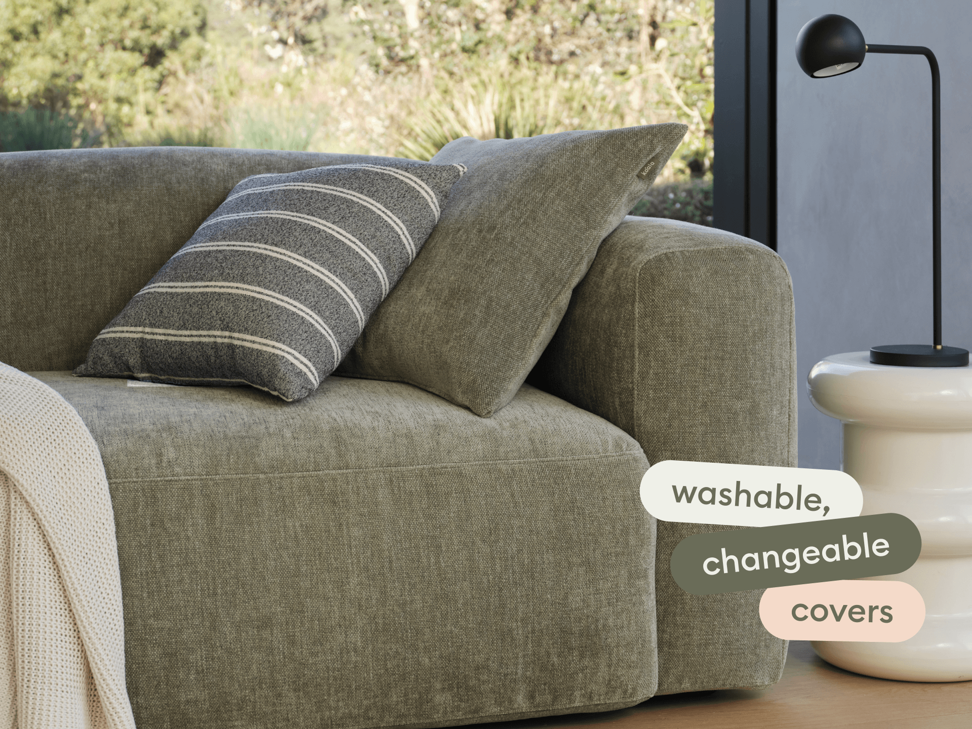 Luxurious olive-green sofa with soft, textured fabric. Features include a low profile and plush cushions. Set in a light-filled, modern living space.