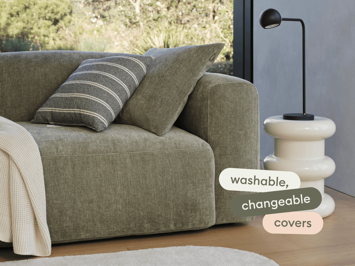 Plush olive-green fabric sofa with washable, changeable covers; paired with an off-white ceramic side table in a modern living room, natural light.