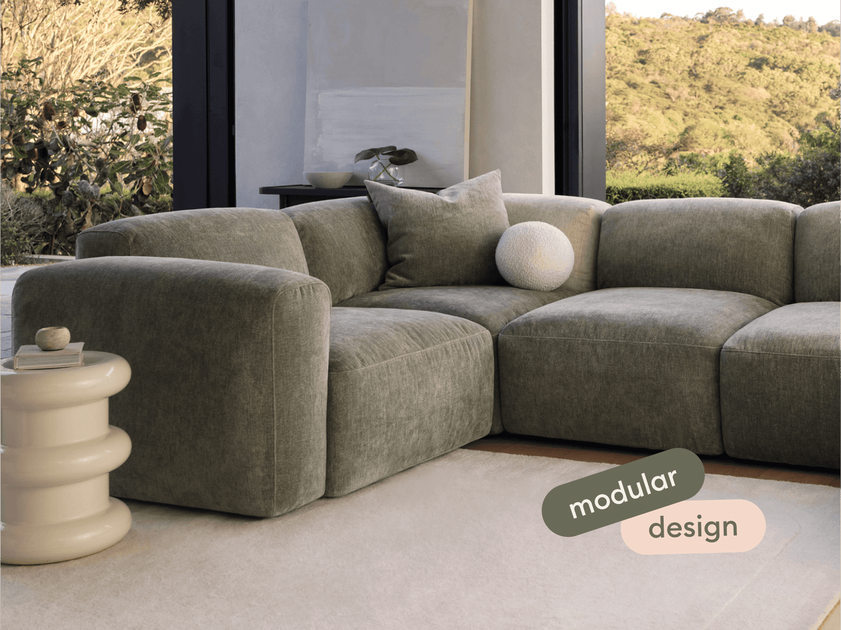 Luxurious green velvet modular sofa with plush cushioning, set in a light-filled modern living room, complemented by a sculptural cream side table.