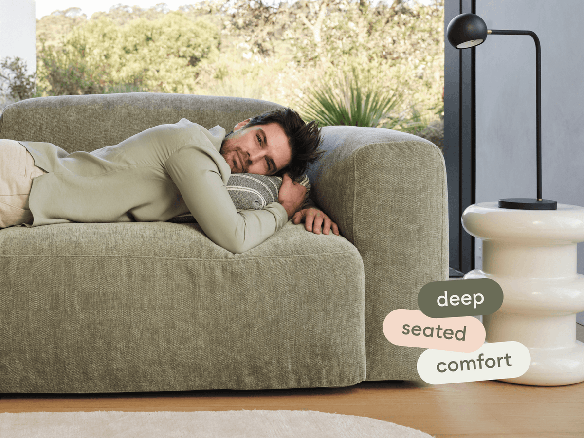 Luxurious olive green sofa with deep seating and plush fabric. Set in a modern living room with natural light and a sleek white side table.