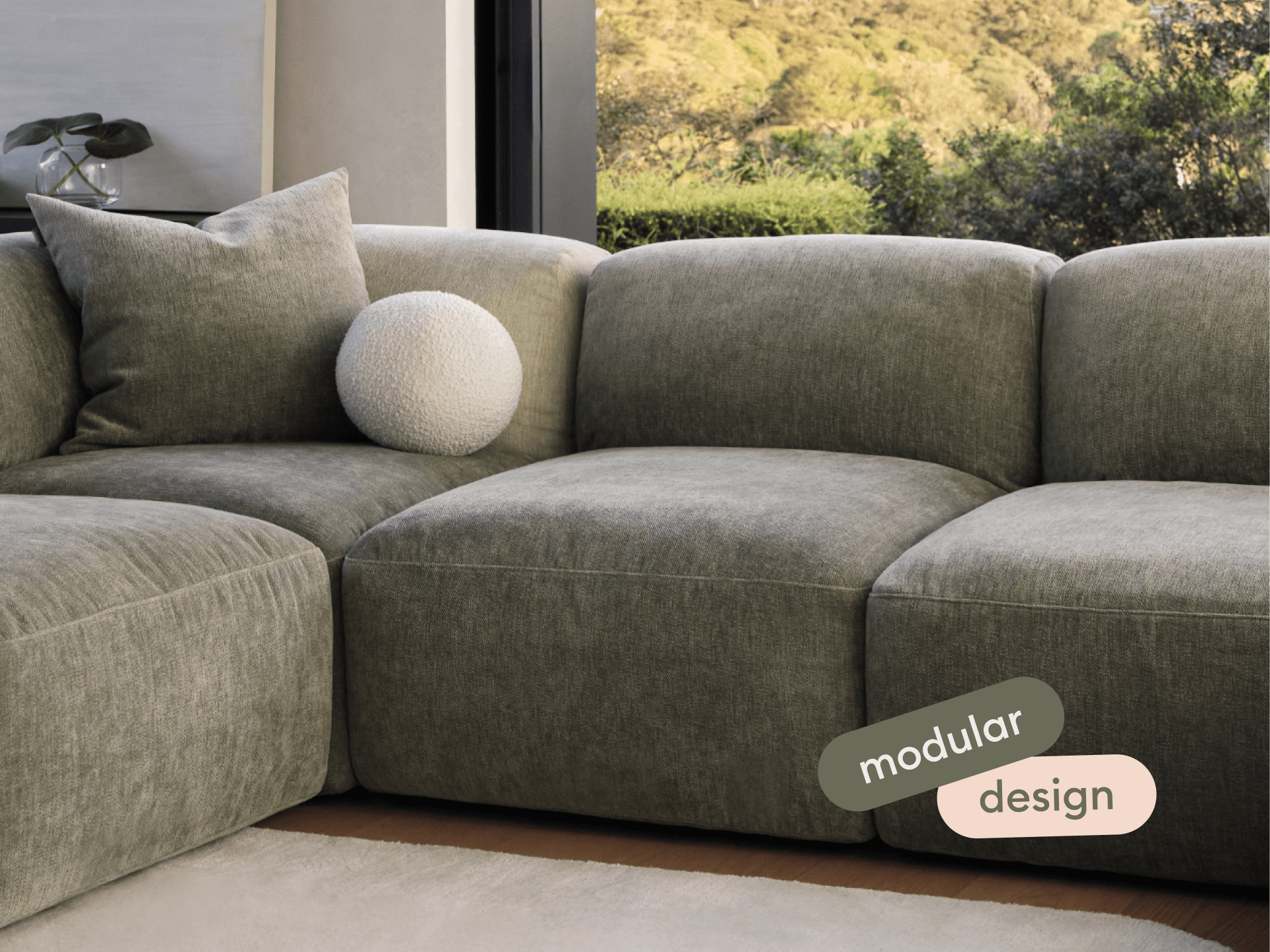 Luxurious modular sofa in soft grey fabric, featuring plush cushions and sleek lines. Positioned in a modern living room with large windows and garden views.