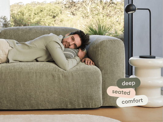 Luxurious olive green sofa in plush fabric, featuring deep seating and rounded arms. Set in a bright modern living room with a sleek white side table.