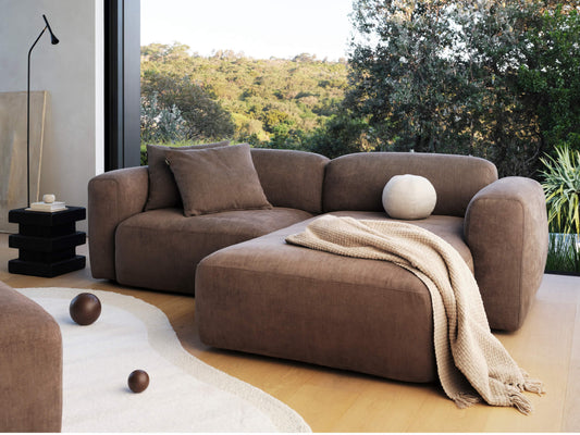 Luxurious brown suede sectional sofa in modern living room, featuring plush cushions and sleek lines. Beige throw adds elegance amidst serene outdoor views.