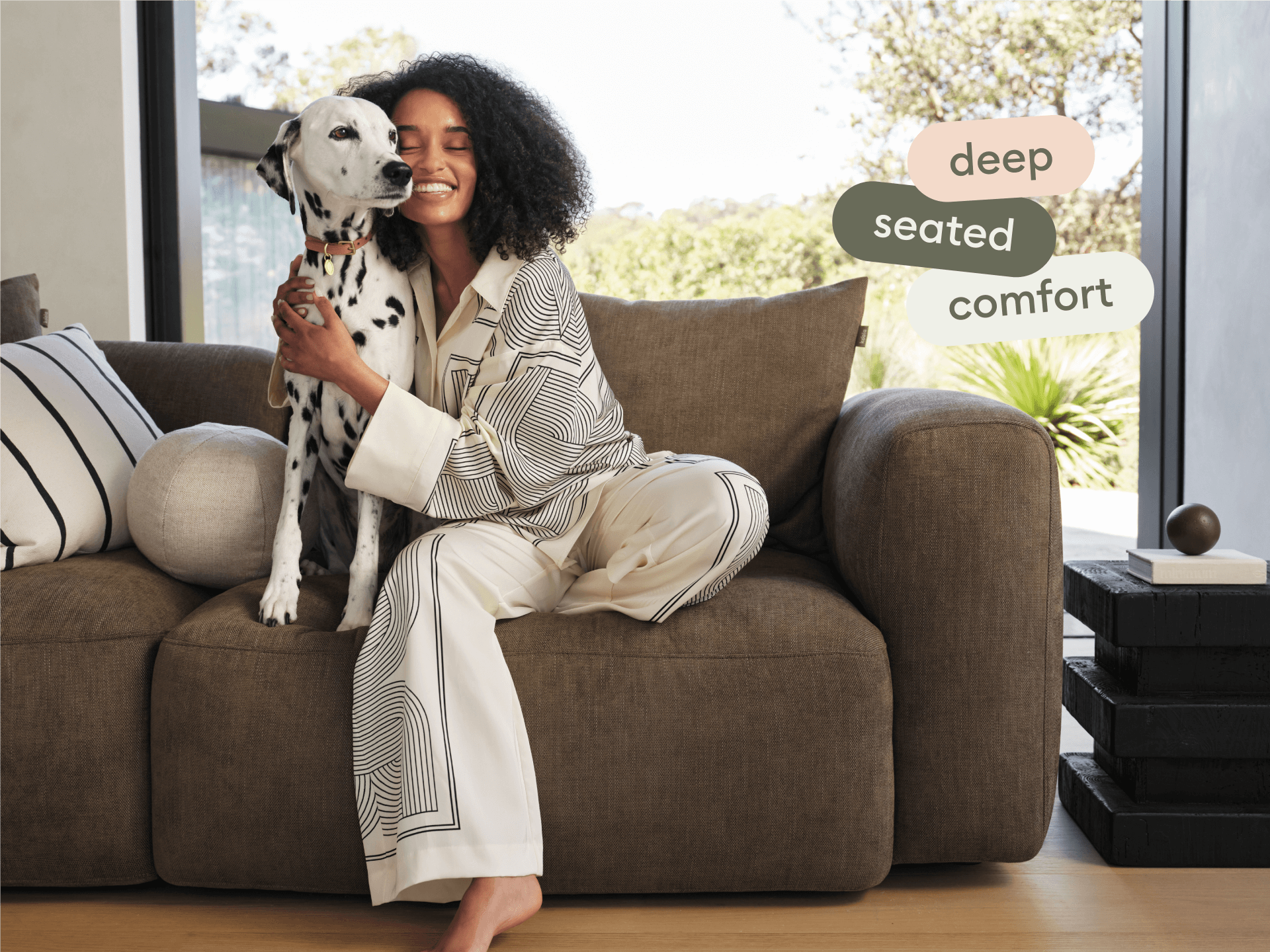 Luxurious deep-seated sofa in rich brown fabric, featuring plush cushions and curved armrests. Set in a bright, modern living room with natural light.