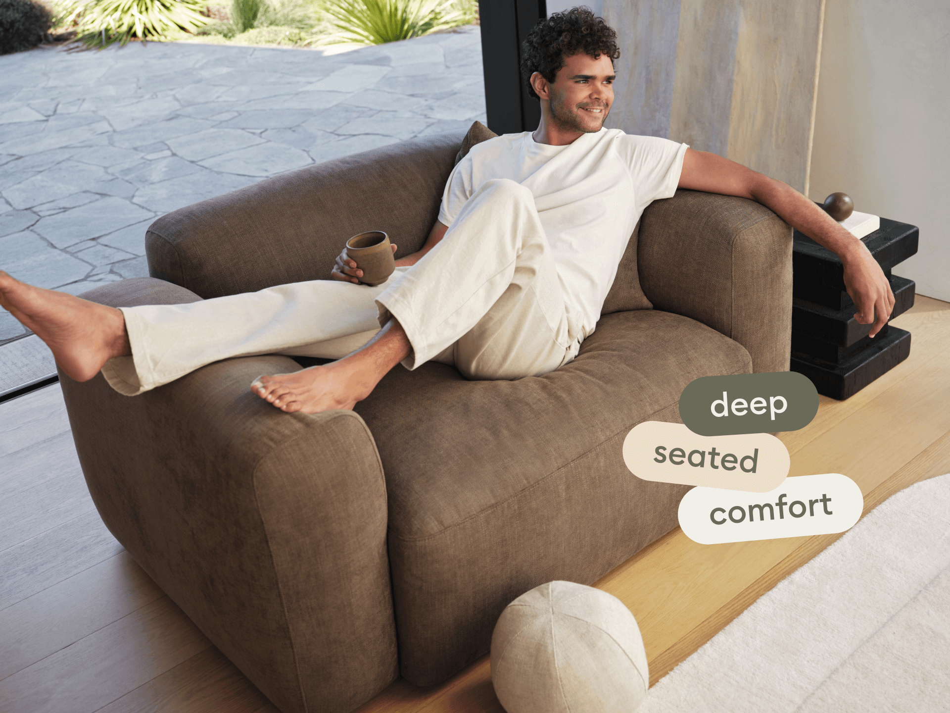 Luxurious deep-seated armchair in rich brown suede, featuring plush cushioning and wide armrests. Set on elegant hardwood flooring by a glass patio door.