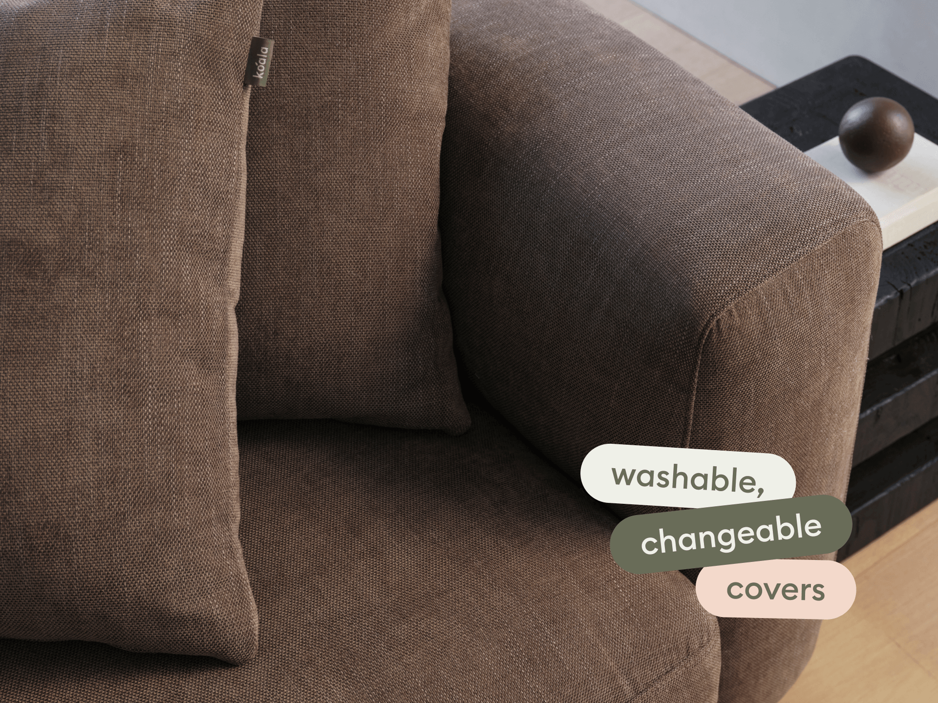 Luxurious brown fabric sofa with washable, changeable covers. Features plush cushions and sleek lines. Positioned against a modern, minimalist interior.