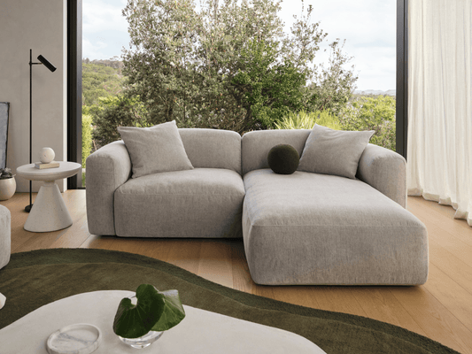 Luxurious grey linen modular sofa with plush cushions, featuring a spacious chaise in a light-filled modern living room. Accented by a marble coffee table.