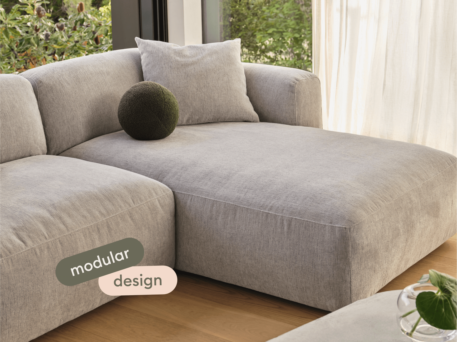 Luxurious grey linen modular sofa with plush cushioning, showcasing clean lines and a modern aesthetic, set in a sunlit living room with wooden floors.