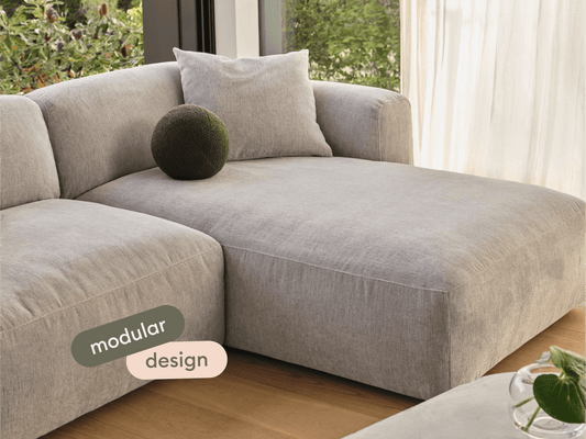 Luxurious grey linen modular sofa with plush cushioning, showcasing clean lines and a modern aesthetic, set in a sunlit living room with wooden floors.