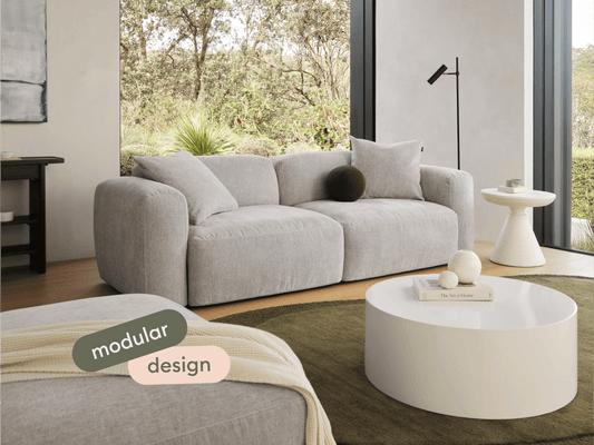 Luxurious modular sofa in soft grey fabric, featuring plush cushions and a contemporary silhouette. Set in an elegant living room with expansive garden views.