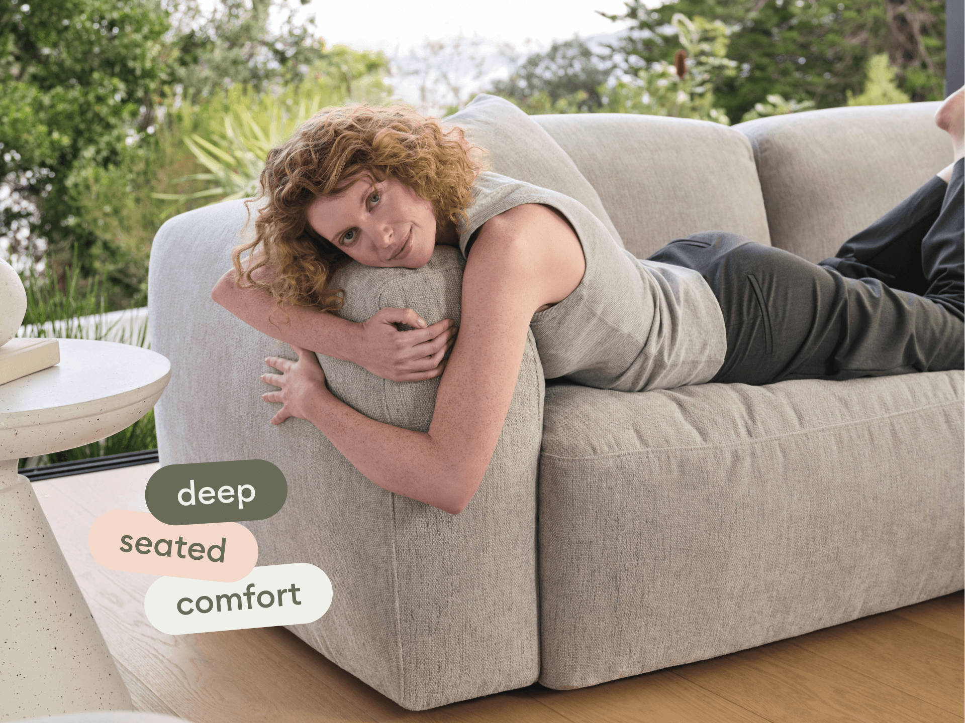 Luxurious grey fabric sofa, featuring deep seating and plush cushions, set against a serene indoor-outdoor backdrop with natural light and hardwood floors.