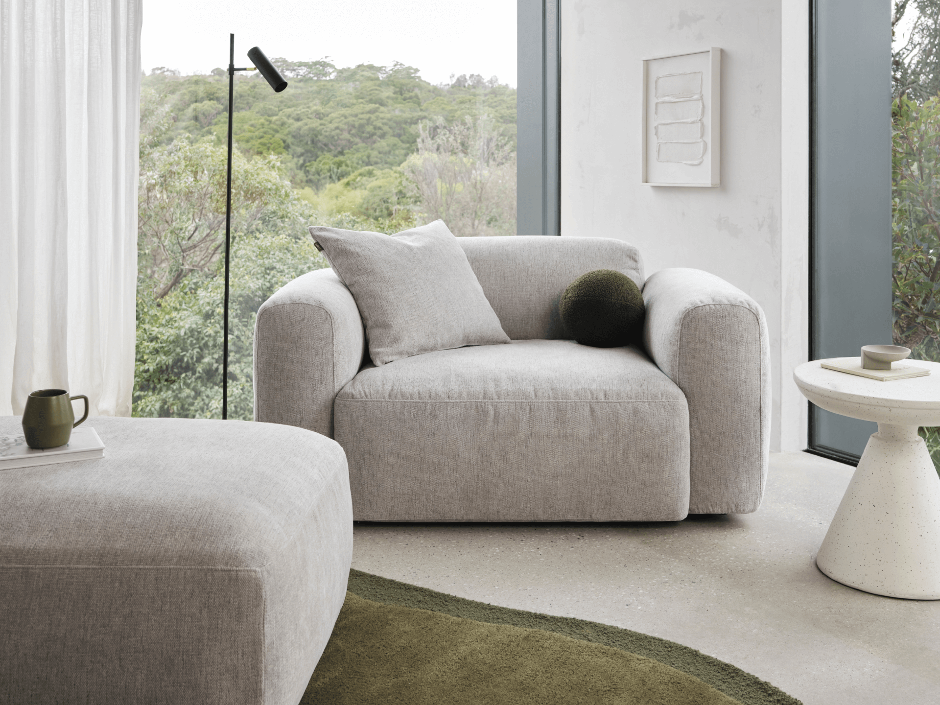 Luxurious grey linen armchair with plush cushions, set in a minimalist living room. Features a high back and wide armrests, complemented by a round side table.